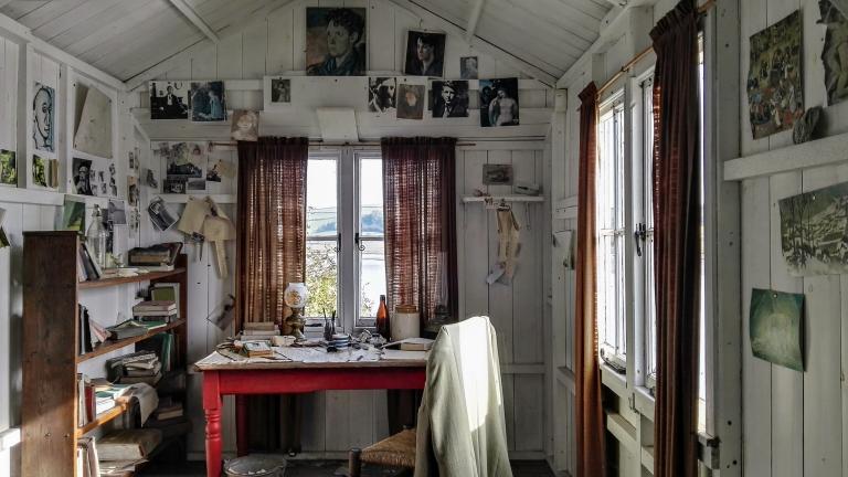 An inside scene of a shed with a writing desk and photographs on the wall.