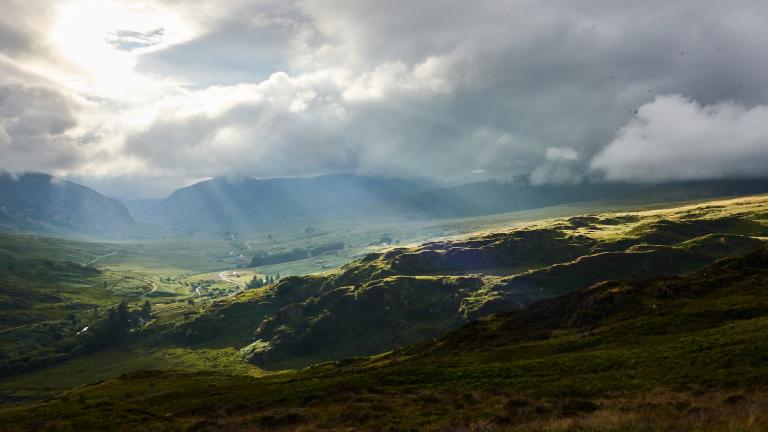 View of sun rays shining through clouds over hilly countryside