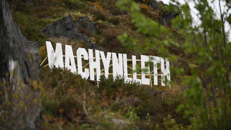 Large white wooden letters spell out "Machynlleth" on the side of a hill