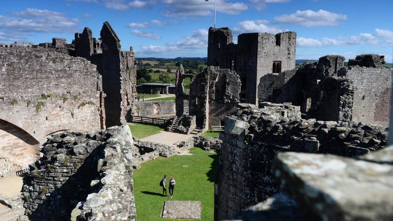 Raglan Castle from above, with two people walking through the ruins.