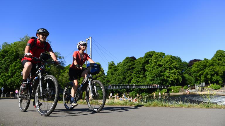 Zwei Fahrradfahrer auf dem Taff Trail in Cardiff mit einer Brücke im Hintergrund.