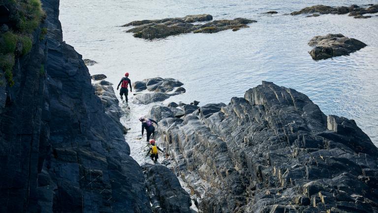 3 people climbing over rocks coasteering