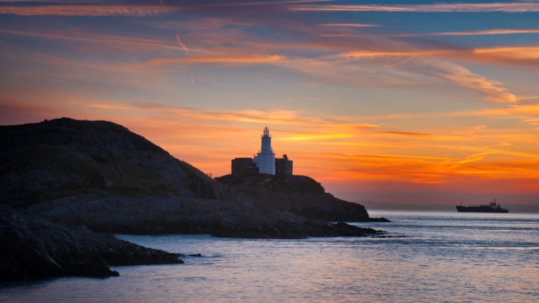 Der Mumbles Head Leuchtturm bei Sonnenaufgang von der Bracelet Bay aus.