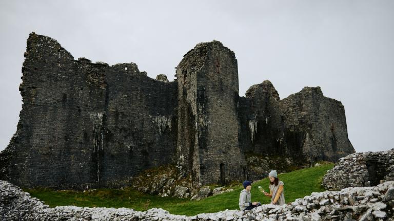 Exterior view of Carren Cennen Castle with two people in the foreground.