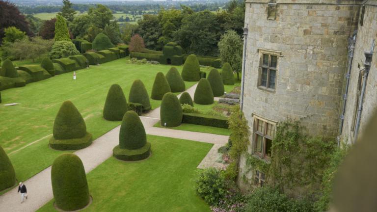 Exterior of Chirk Castle with greenery growing up tower and garden with topiary.
