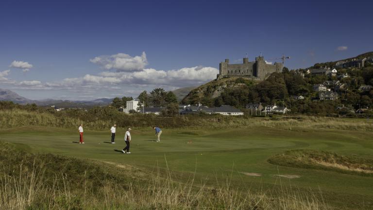 Four people playing golf at Royal St. David's Golf Club with Harlech castle above.