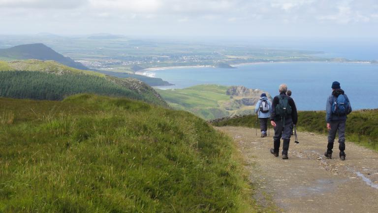 Three walkers on a coast path with views across a bay.