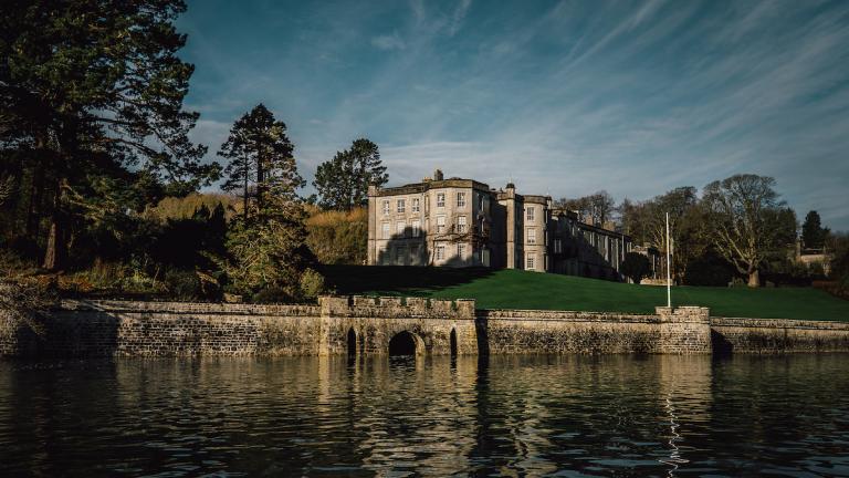 On the water looking at the Plas Newydd building with blue sky behind and green trees surrounding.
