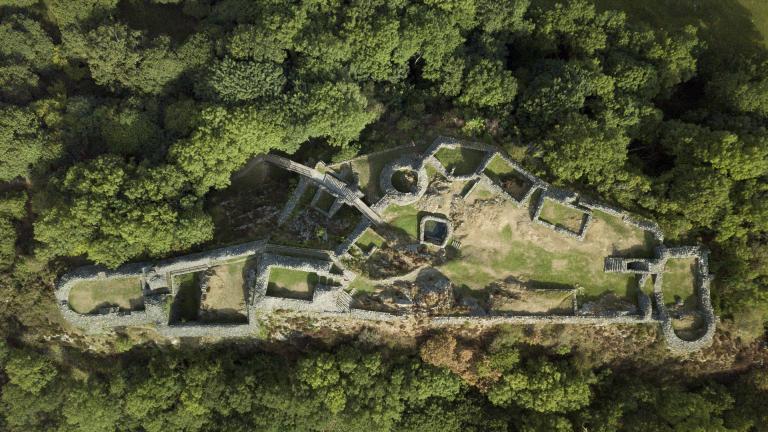 A ruined castle surrounded by woodland from above.