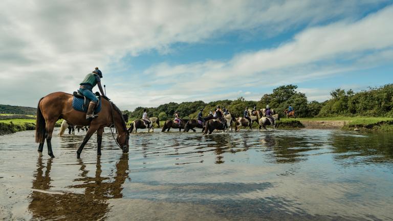 A group of riders on horses crossing a river.