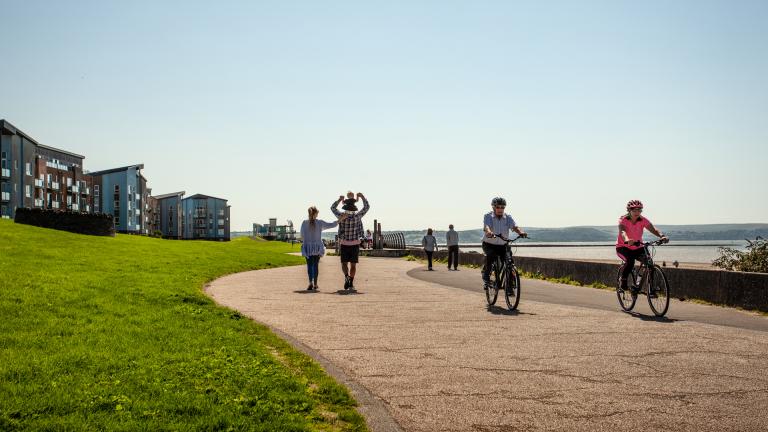 Walkers and cyclists on a wide seafront pathway.
