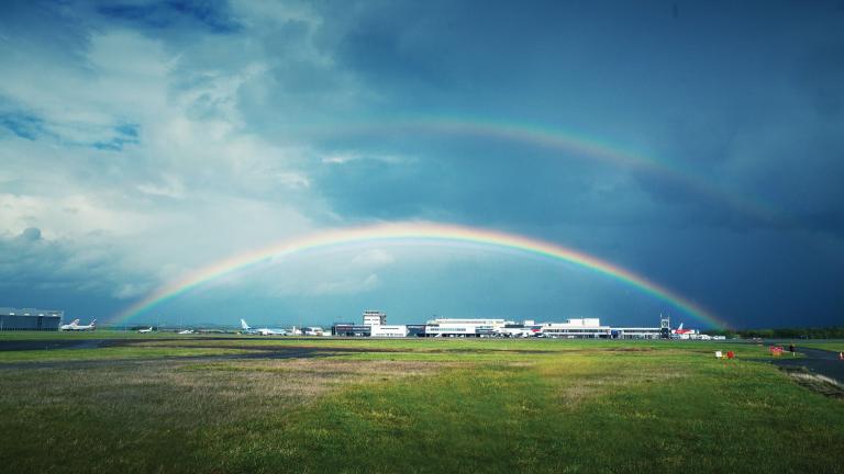 Rainbow over the landing field at airport and white buildings in background.