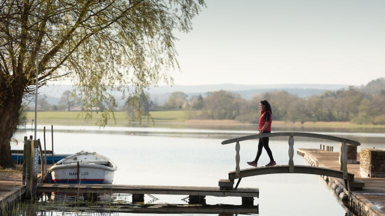 Woman walking across a bridge over a lake.