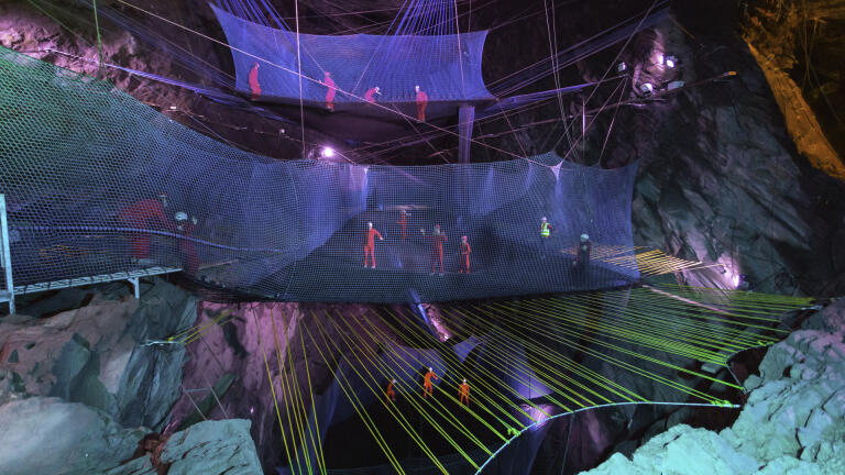 People bouncing on trampoline-style nets in an underground slate cavern