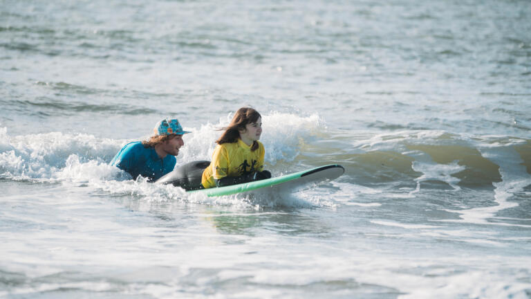 A young lady being helped to use a surfboard. 