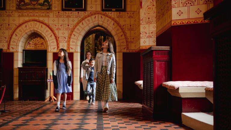 Mutter und zwei Kinder bestaunen die üppige Decke eines prunkvollen Raumes in einer Burg