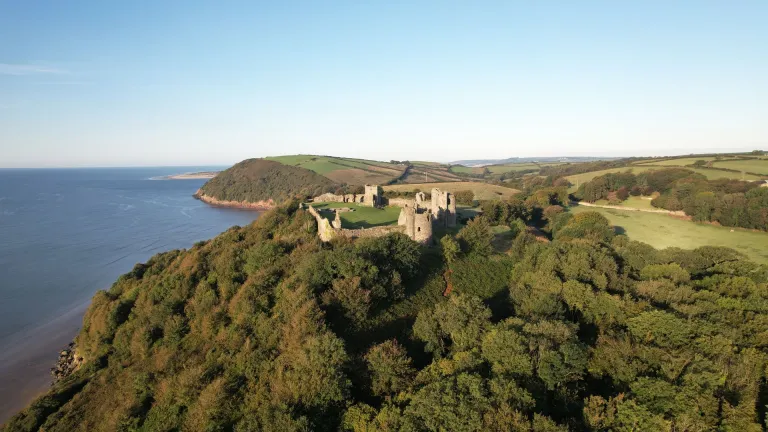 Aerial view of castle  high above coast with views of sea and countryside.
