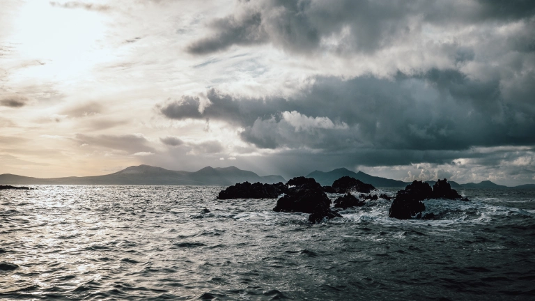 Moody seas with rain, rocks and sunshine breaking through.