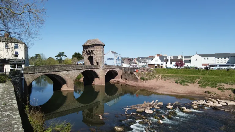 An ancient stone bridge over a calm river, with a tower in the middle.