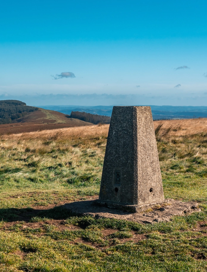 A stone plinth at the top of a mountain with far reaching views.