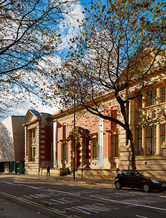 A red and sand brick building, home to an art gallery on a tree lined road.