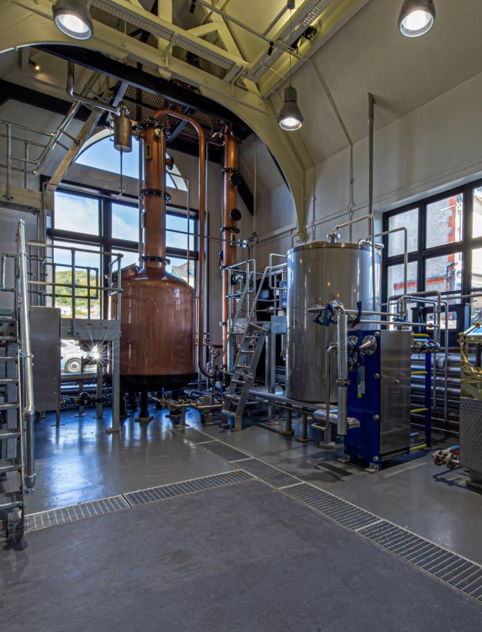 A large copper vat and distilling equipment in a building with large windows.