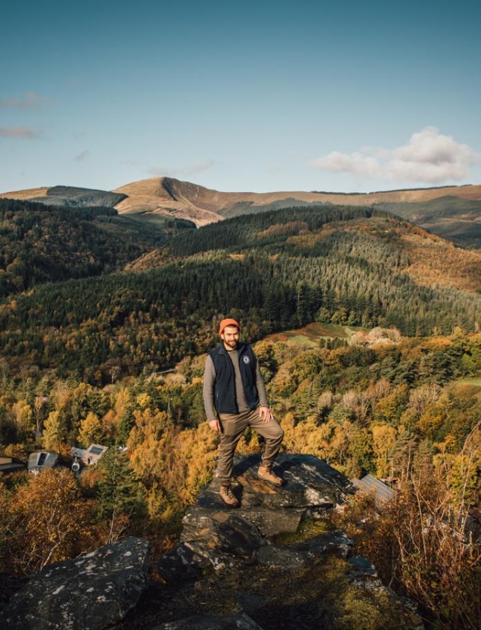 Ein Mann steht auf einem Bergrücken mit der Landschaft im Hintergrund.
