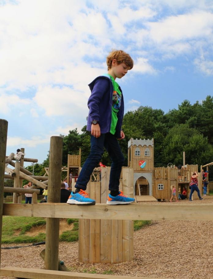 11 year old boy walking across a plank in an adventure playground