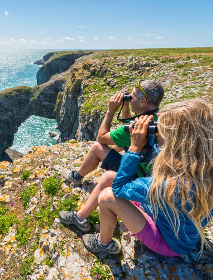 A couple on the coast path looking out to sea with binoculars.