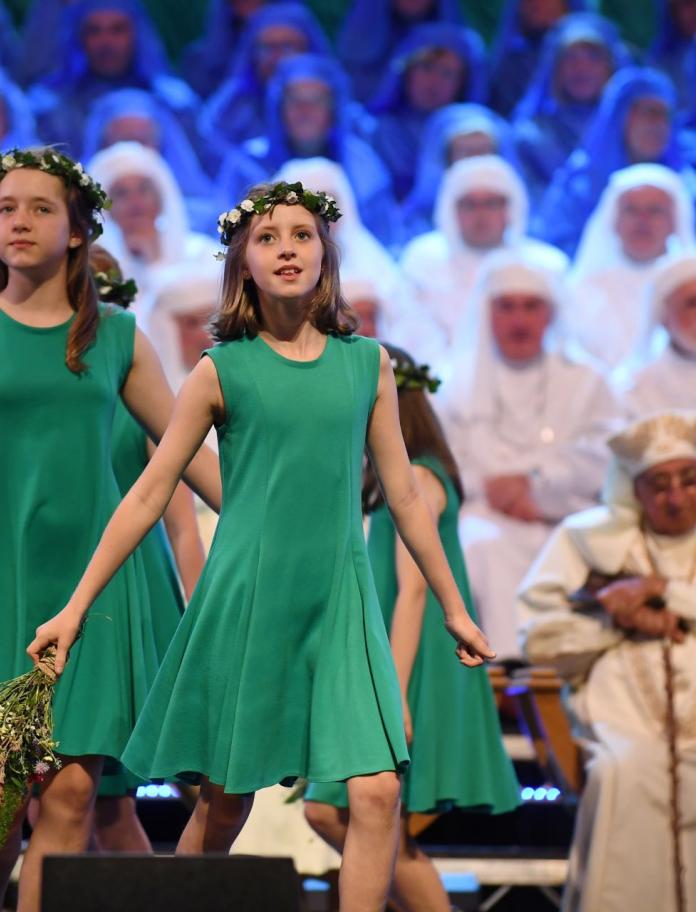 Young dancers wearing green dresses and a ring of flowers laid on their head performing at a festival.