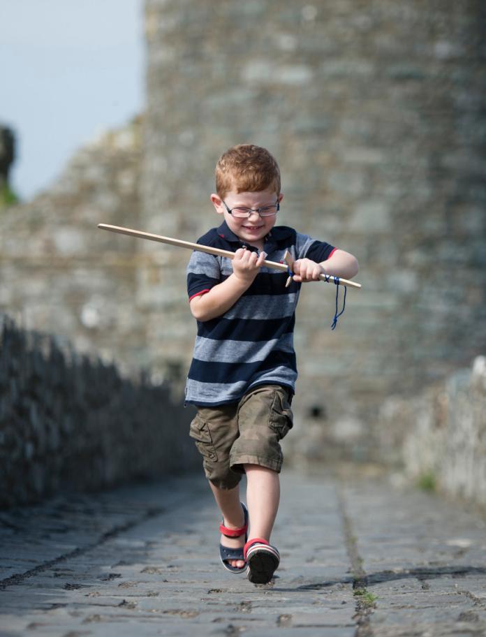 Little boy running through Harlech Castle with pretend wooden sword