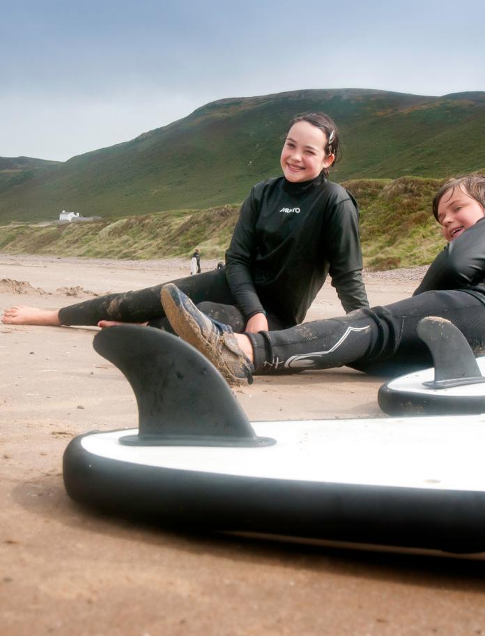 Boy and girl resting on beach after surfing Rhossili