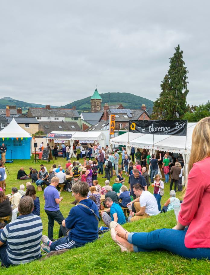 People sitting on a grass verge overlooking stalls at the food festival
