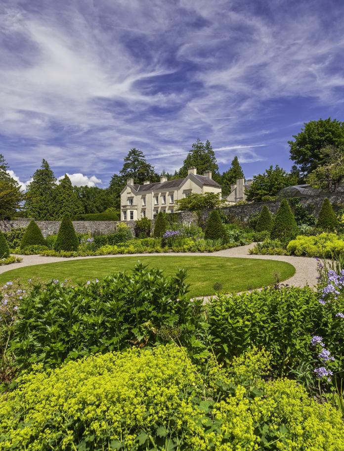 A view of Aberglasney House surrounded by the garden with dramatic blue sky and wispy clouds.