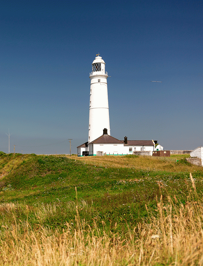 A white lighthouse on a cliff edged coastline.
