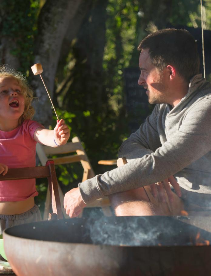 A girl holds a marshmallow over an open fire.