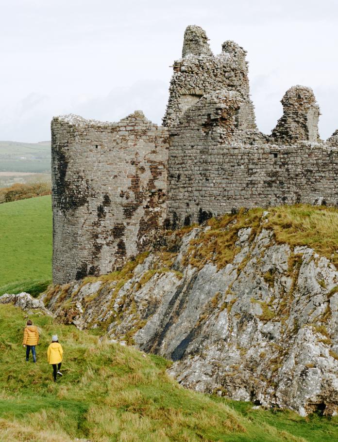 Two people exploring external stone walls of Carreg Cennen Castle.