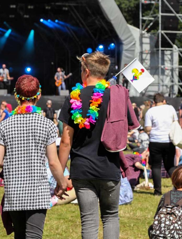 Couple holding hands walking towards live music, Pride Cymru.