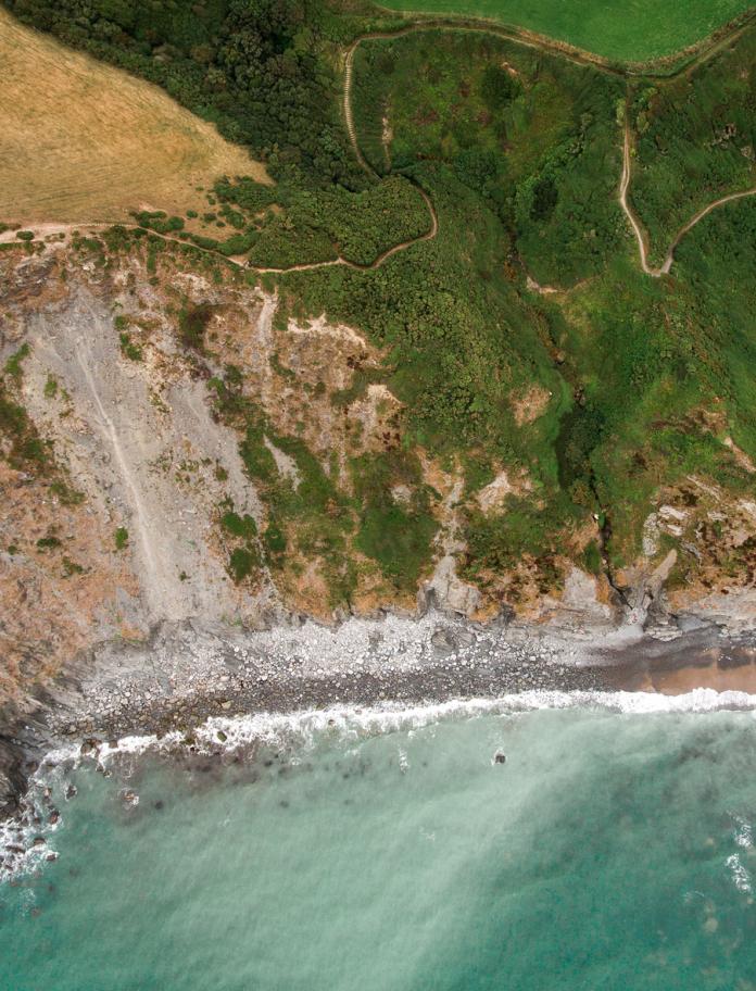 Luftaufnahme eines Pfades an einer Küstenlinie mit dem Meer im Vordergrund.