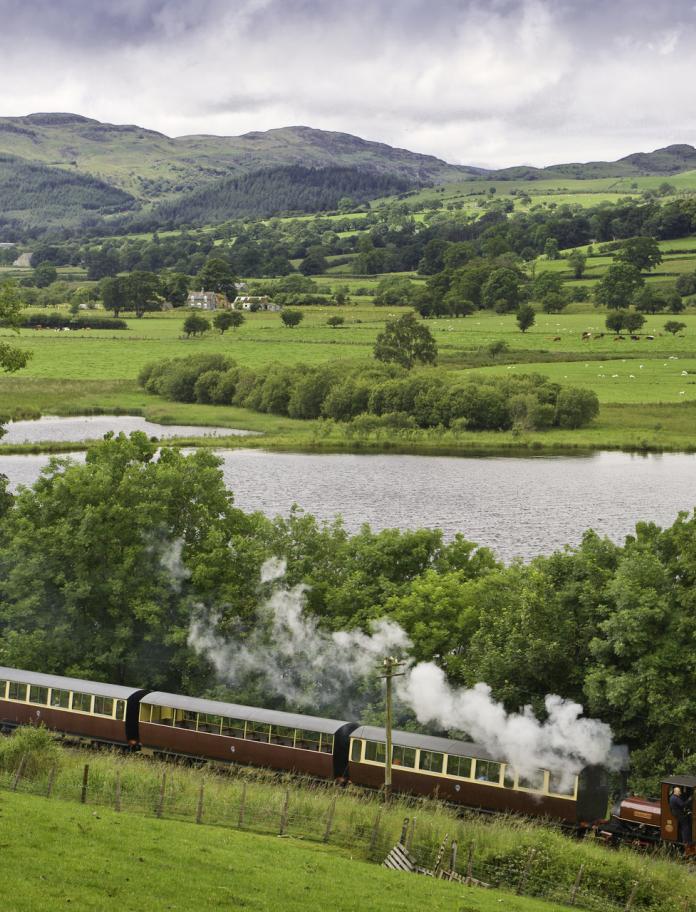 Bala Lake Railway steam train travelling along the lakeside with mountains in the background.
