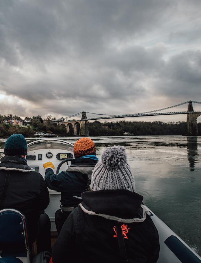 People on a boat with Menai Suspension Bridge in the distance