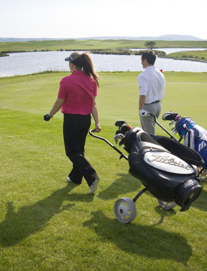 A lady and gentleman golfer walking to the next tee with golf trolleys at Machynys Golf Club.