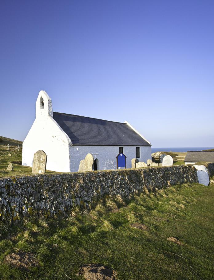A small white church and graveyard isolated amongst the coastline and fields.