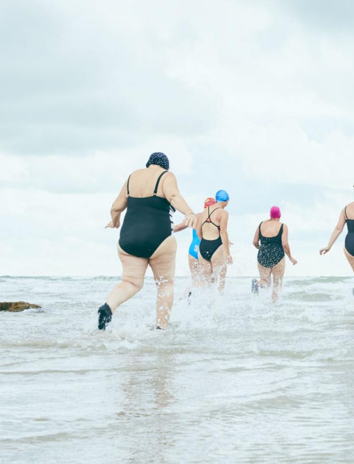 Group of women with their backs to camera running into the sea.