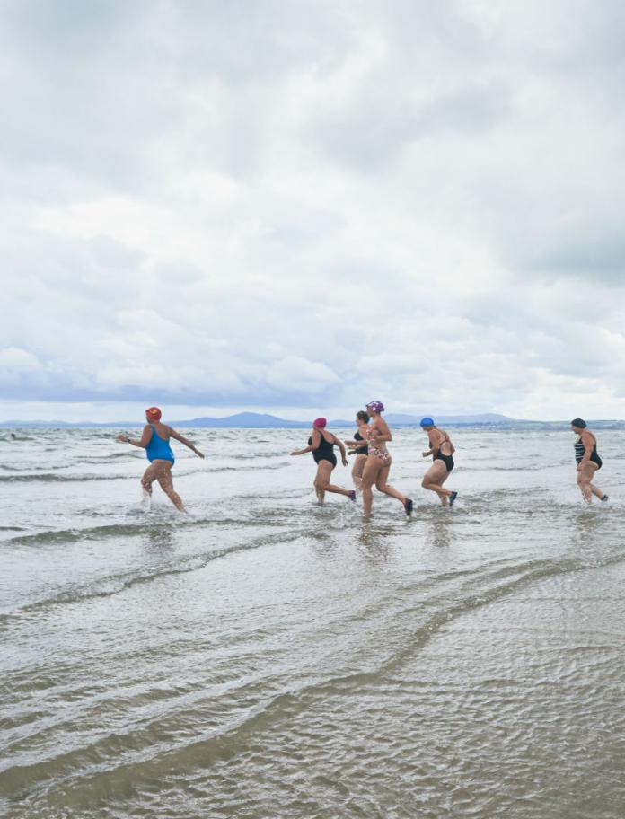Image of women in swimming costumes running into the sea.