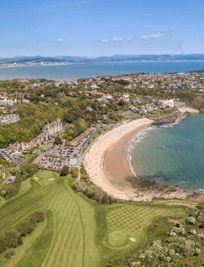 Aerial shot of a golf course and coastline in the sunshine.