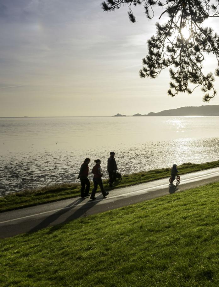 Cyclist and walkers on Coast Path at Blackpill at sunrise with Mumbles in background