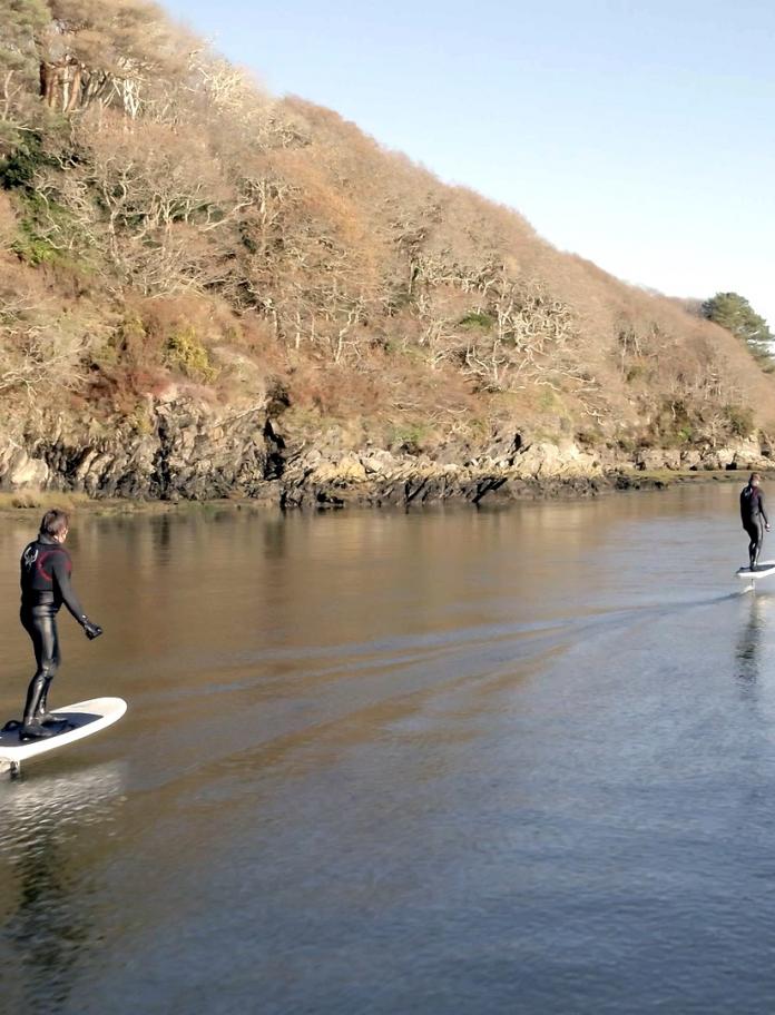 Two people using eFoil surfboards on a river.