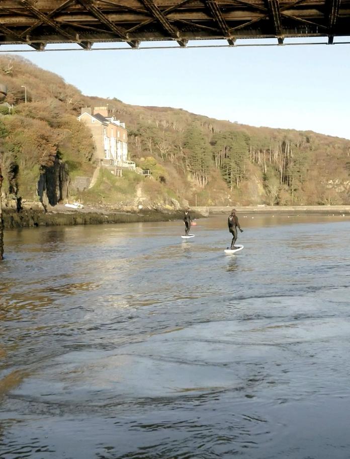 Two people using eFoil surfboards on a river.