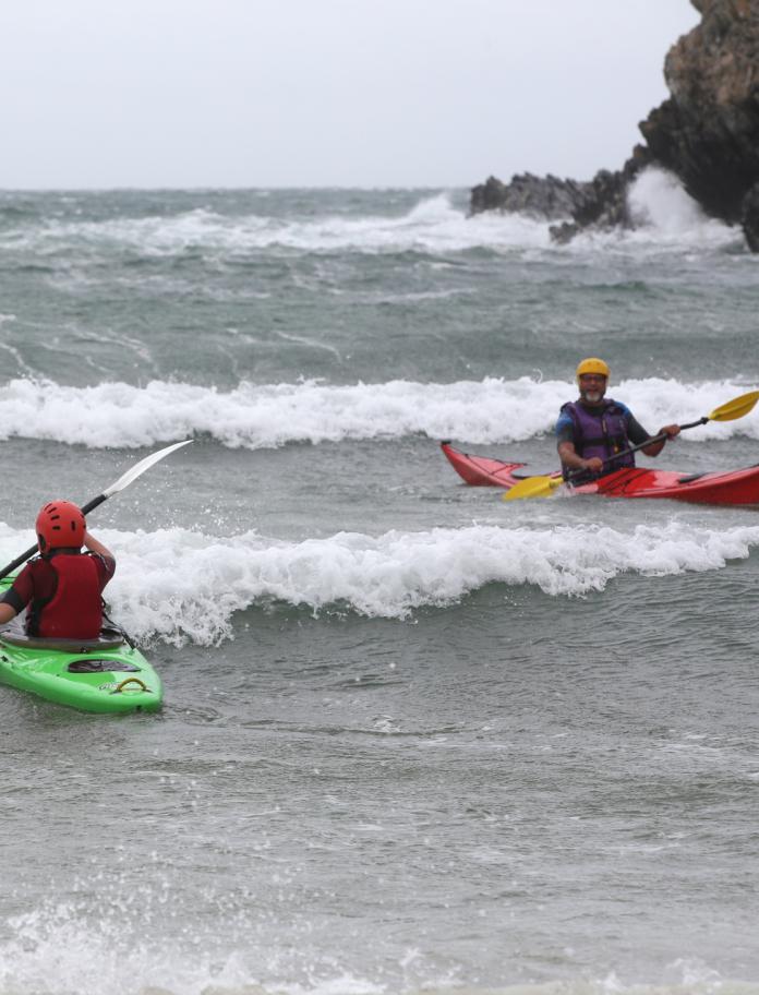 Two people kayaking into waves.